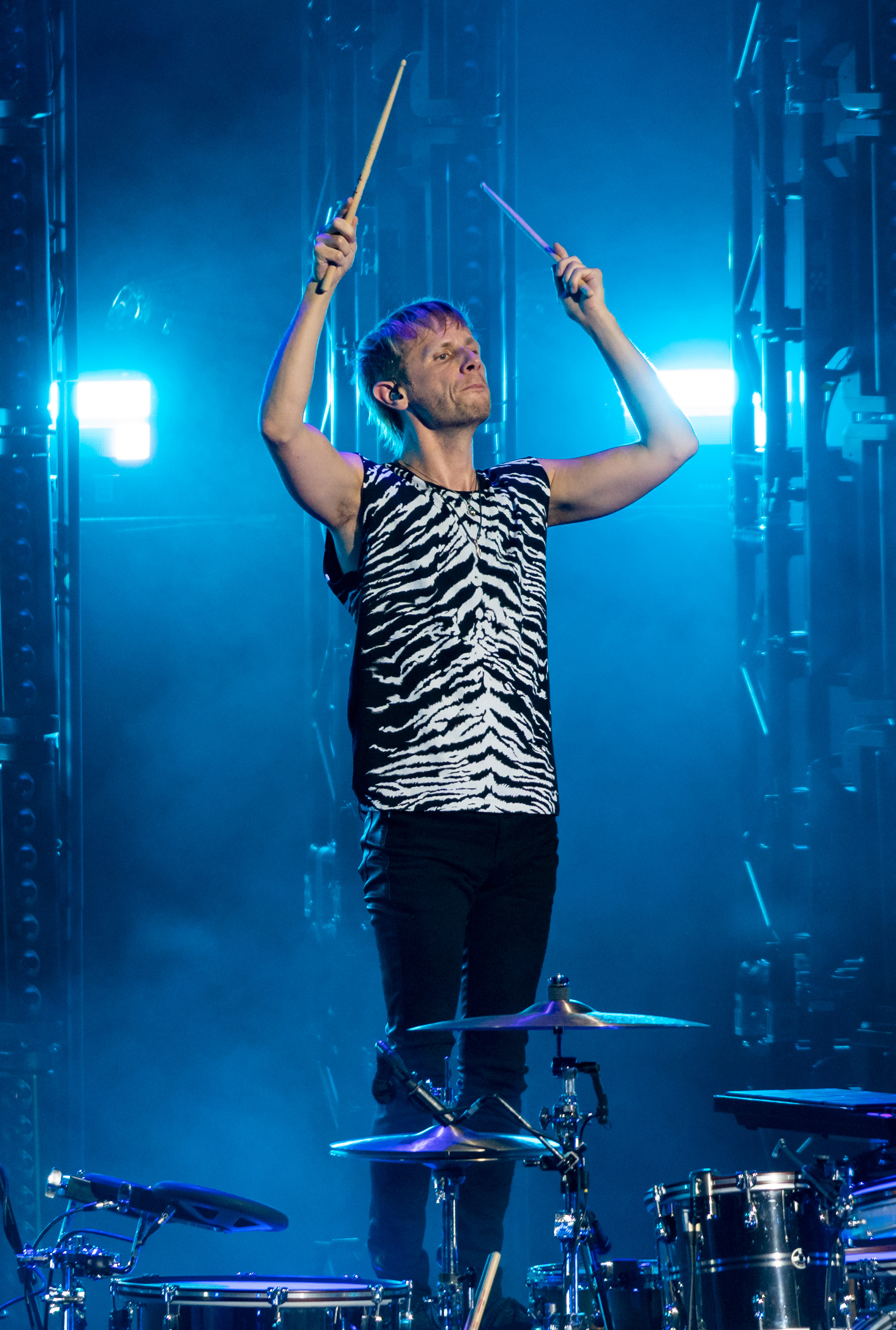 Dominic Howard standing on his drum stool holding drum sticks